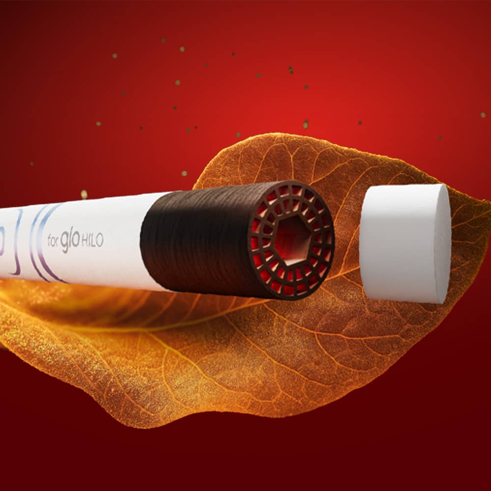 A close-up of a vape pen with its cap removed, revealing a honeycomb-patterned heating element. The pen is placed above a dried tobacco leaf, set against a deep red background.