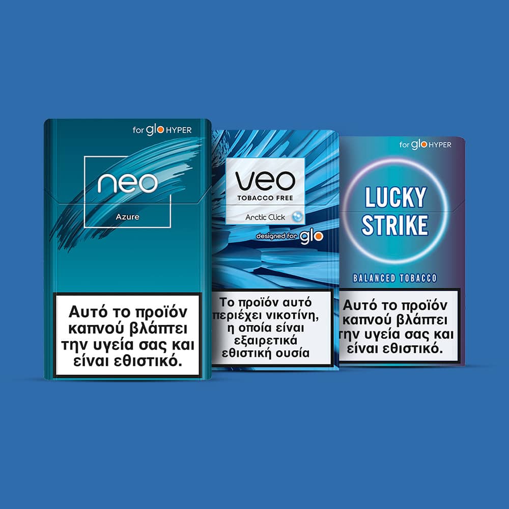 Three cigarette packs (Neo Azure, VEO Arctic Click, Lucky Strike Balanced Tobacco) stand side by side, each with a Greek health warning label stating smoking harms your health and is addictive. Blue background.