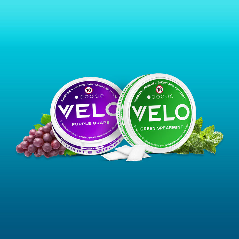 Δύο στρογγυλά κουτάκια VELO FREE SAMPLE - ένα μωβ σταφύλι με σταφύλια και ένα πράσινο δυόσμο με φύλλα μέντας - είναι τοποθετημένα σε μπλε διαβαθμισμένο φόντο, αναδεικνύοντας το VELO ως το ελληνικό προϊόν της χρονιάς 2025.