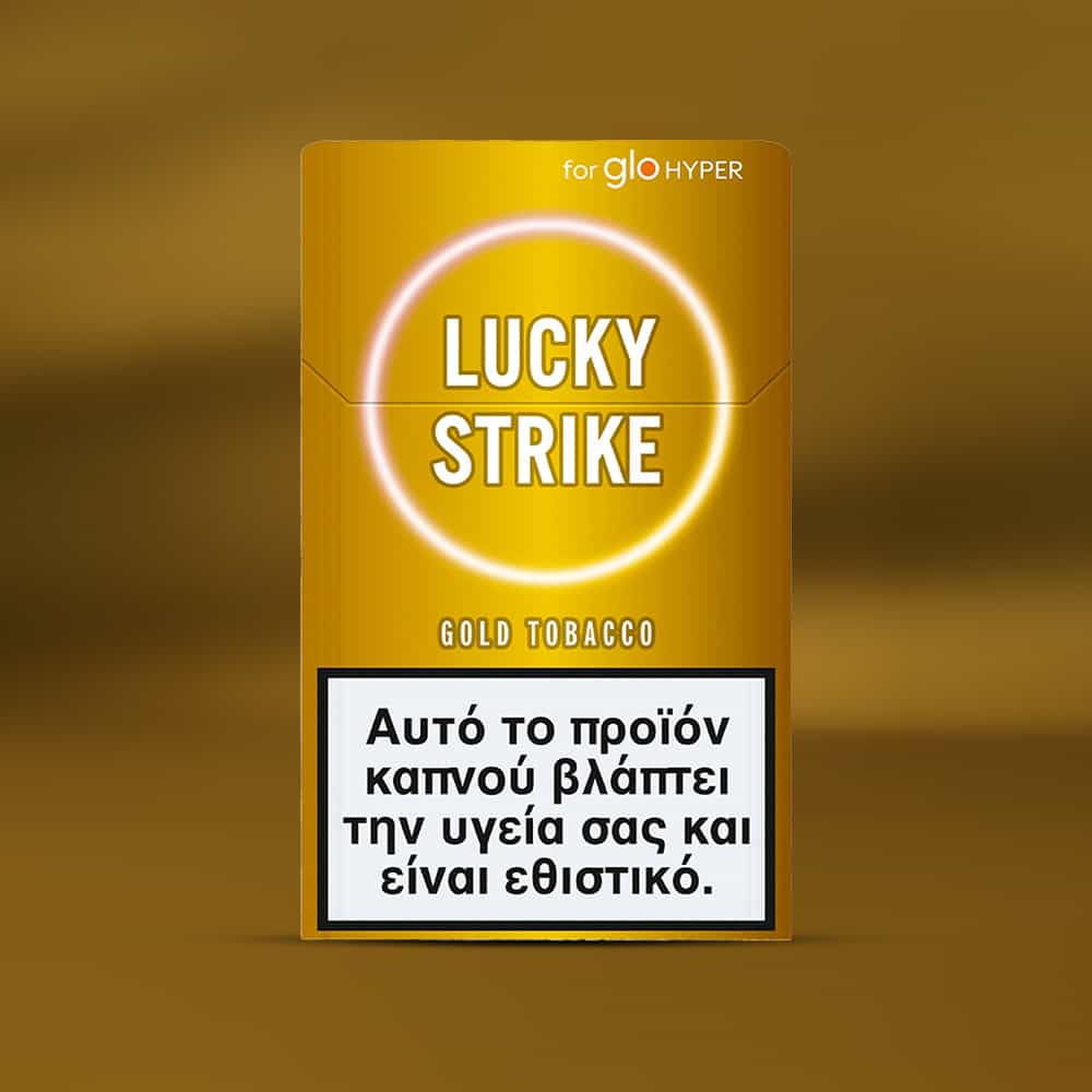A gold Lucky Strike Gold Tobacco pack for glo HYPER is displayed, with a Greek health warning: "Αυτό το προϊόν καπνού βλάπτει την υγεία σας και είναι εθιστικό." Flavor notes suggest nutty tobacco and creamy undertones.