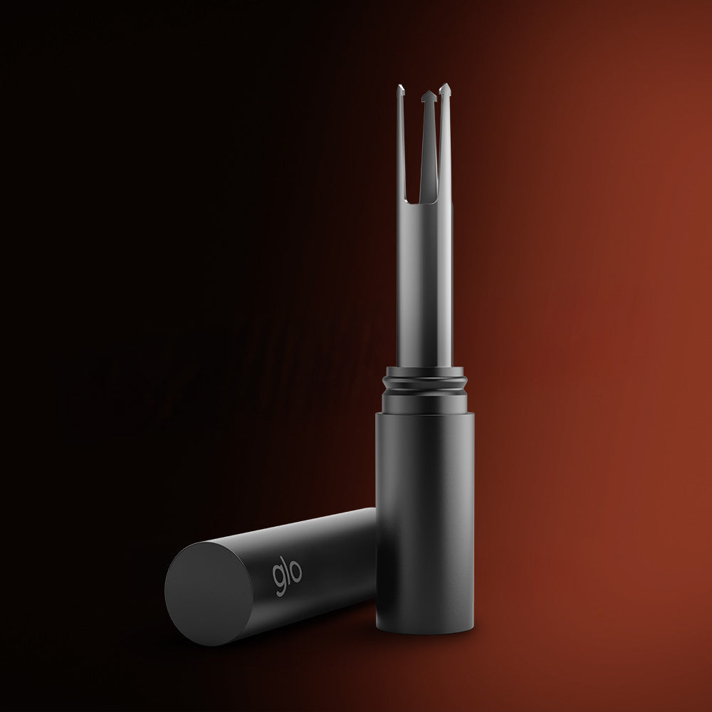 The glo™ HILO Stick Remover, a sleek black cylindrical debris remover with metallic open-ended tip and glo branding, is shown upright with its cap off against a gradient dark brown background.