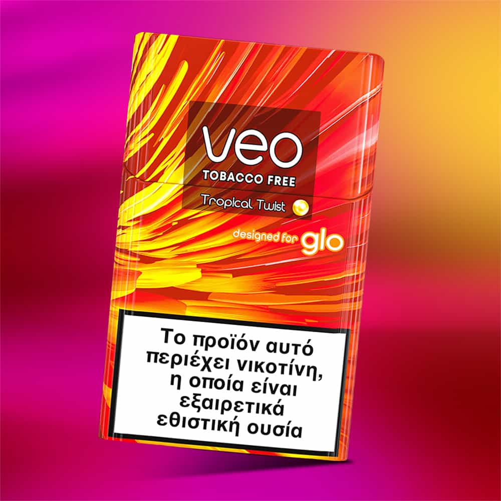 A colorful veo™ Tropical Twist pack designed for glo features a pink and yellow background and a Greek warning at the bottom stating it contains nicotine, a highly addictive substance. The pack is labeled "TOBACCO FREE.
