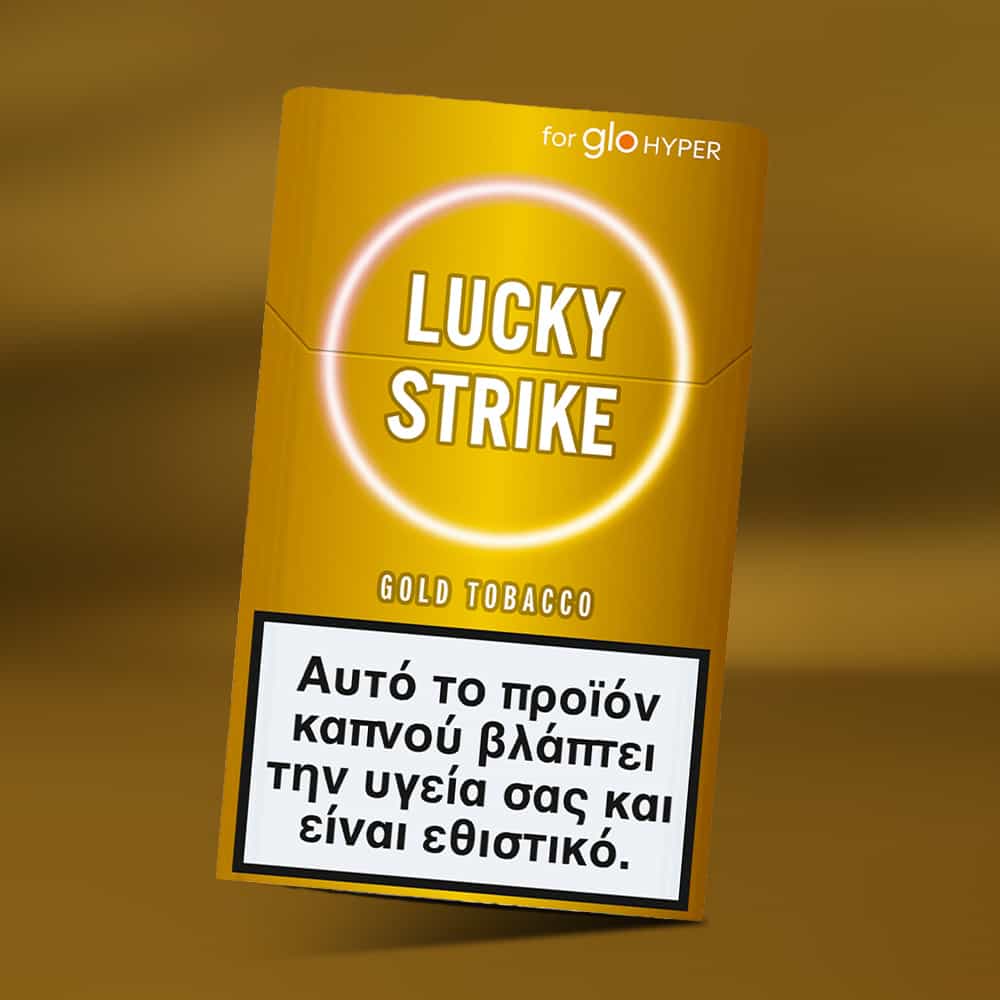 A gold Lucky Strike Gold Tobacco pack features a Greek health warning at the bottom, stating that smoking harms your health and is addictive. The matching gold background hints at nutty tobacco and creamy notes.