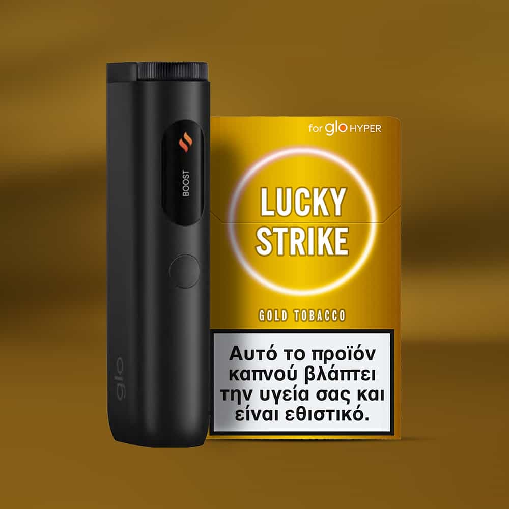 A black electronic device and a yellow Lucky Strike Gold Tobacco pack are displayed. The tobacco, noted for its nutty and creamy notes, features a Greek health warning about smoking risks.