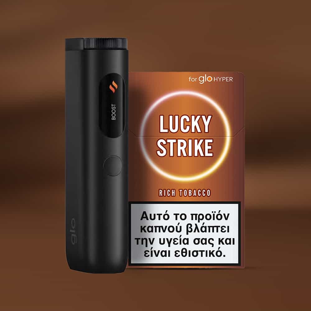 A black Glo Hyper device is beside a pack of Lucky Strike Rich Tobacco, featuring Burley notes and a Greek health warning on the front. The brown background has a soft gradient.