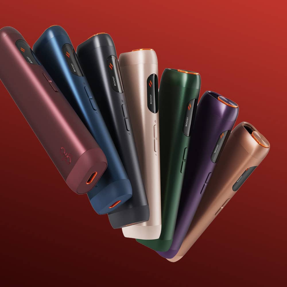 A row of seven sleek, cylindrical glo™ HILO devices with Turbostart technology in red, blue, black, silver, green, purple, and gold stands against a red gradient background—showcasing the advanced new product.