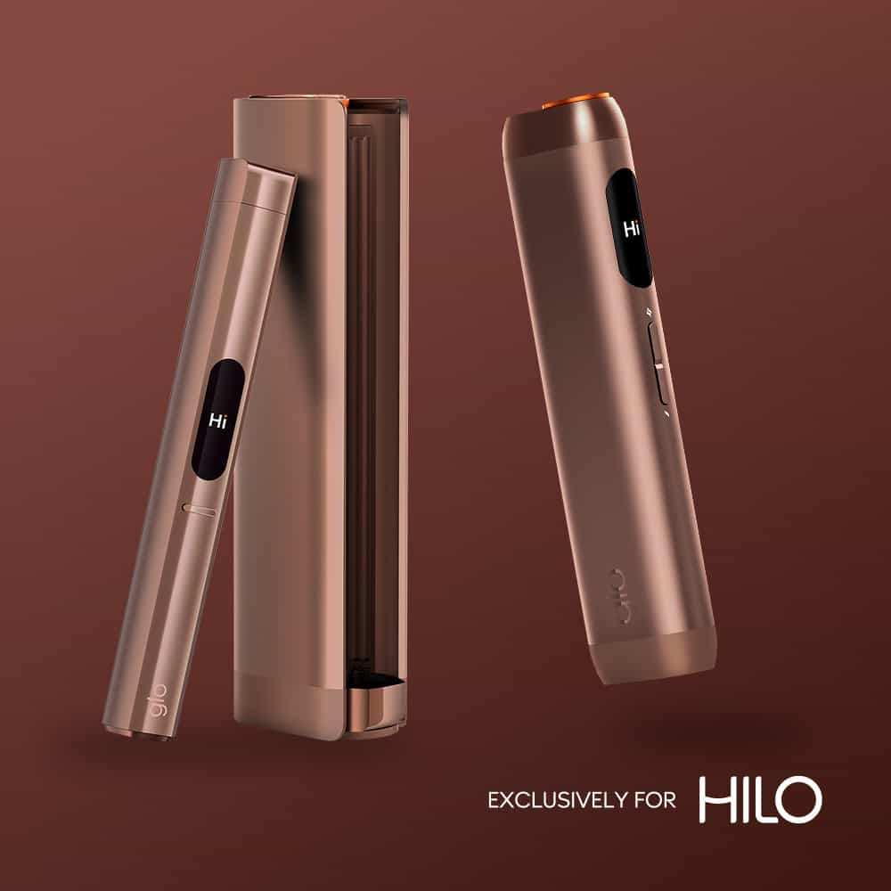 Two sleek, bronze virto™ Classic Tobacco devices with small screens displaying "Hi" are shown against a brown background. One stands upright while the other is partially slid from a case. Text reads: Exclusively for HILO.