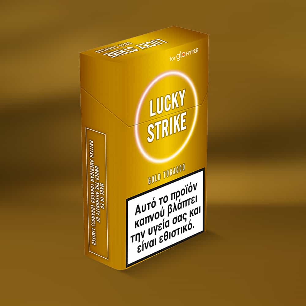 A gold-colored Lucky Strike Gold Tobacco cigarette pack with Greek health warnings, labeled "for glo HYPER" on top, features a profile with creamy notes and hints of nutty tobacco.