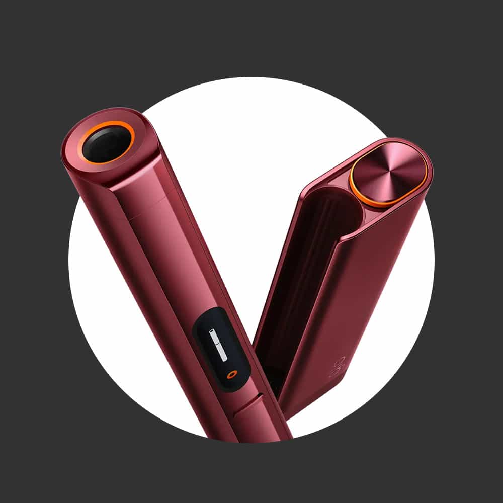 A sleek, metallic red hair styling tool with rounded edges, a digital display, and orange accents, shown slightly open against a white circle with a dark gray background.